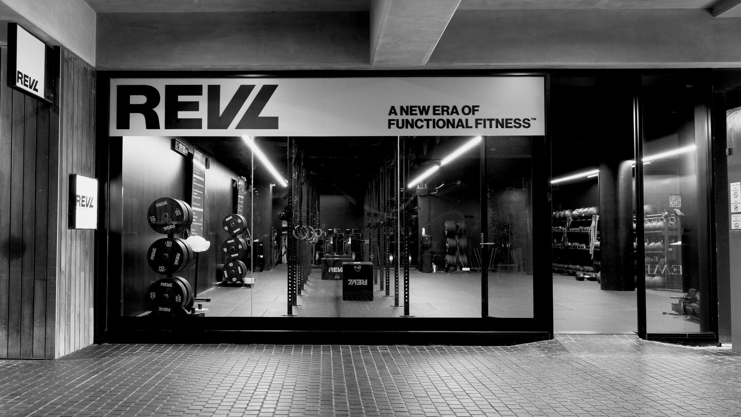 A REVL studio storefront at night, the lit fascia above full-height glass with the training floor inside